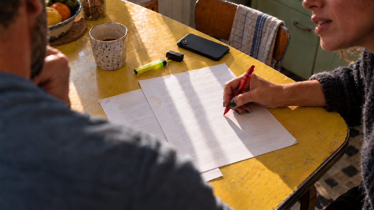 Couple relisant deux offres de prêt annotées au stylo rouge sur une table de cuisine