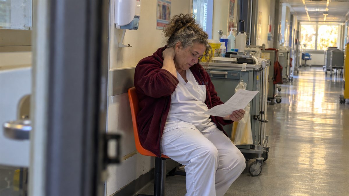 Aide-soignante assise dans un couloir d'hôpital, lisant un courrier en fin de garde